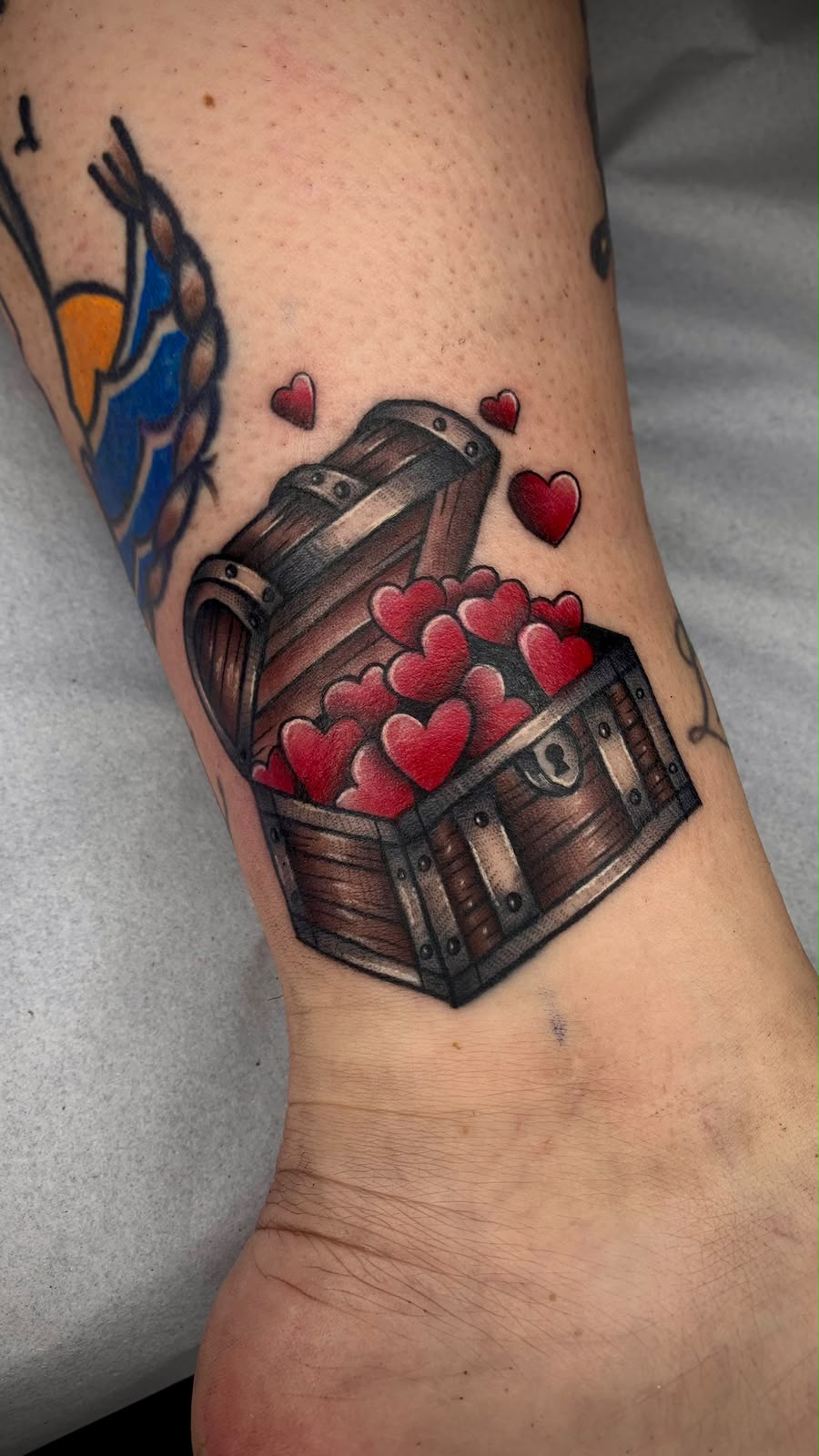 Tatuagem Old School Baú de Corações na região tornozelo feita por Juh Godoy em Porto Alegre