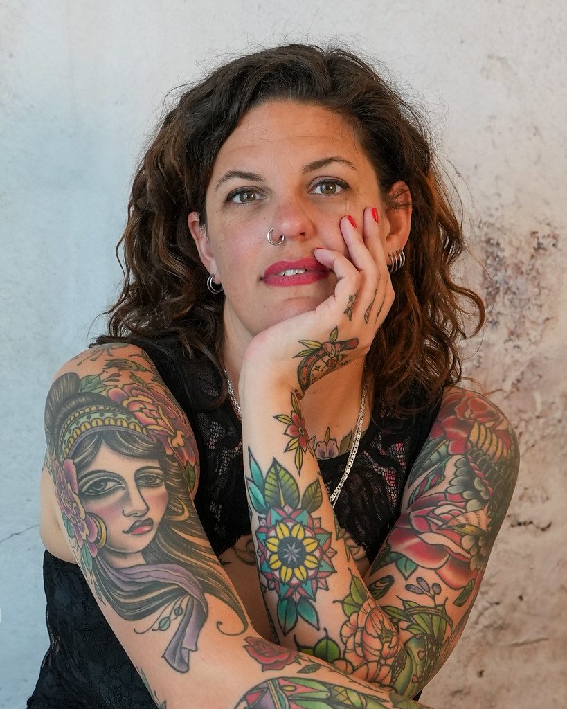Pessoa tatuada sorrindo, com braços fechados em tatuagens coloridas