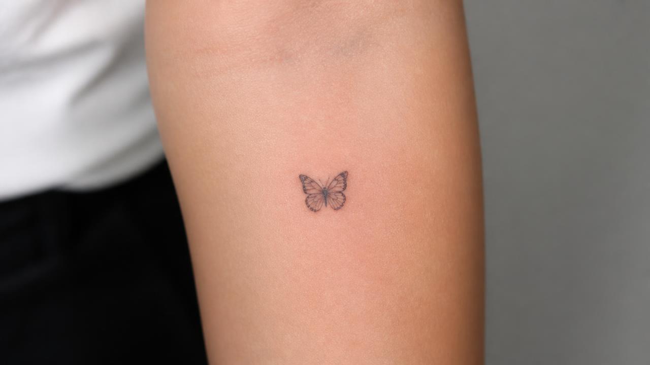 Microtatuagem realista de uma borboleta no antebraço, em escala muito pequena e traço fino